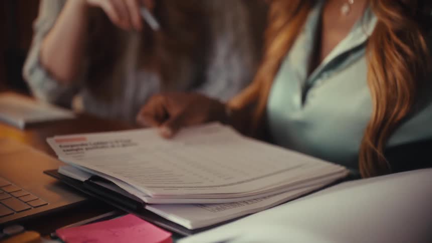Two diverse businesswomen collaborate in slow motion, reviewing charts and graphs together in a warmly lit office
