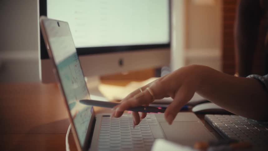 Two diverse female coworkers collaborate while analyzing financial data charts on a laptop screen in a home office