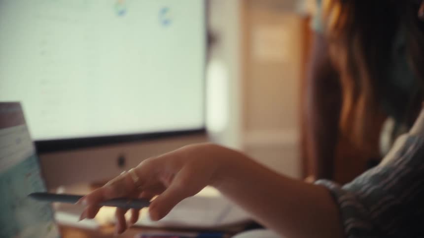 A businesswoman uses a pen to point out details on a financial chart on her laptop while collaborating with a coworker