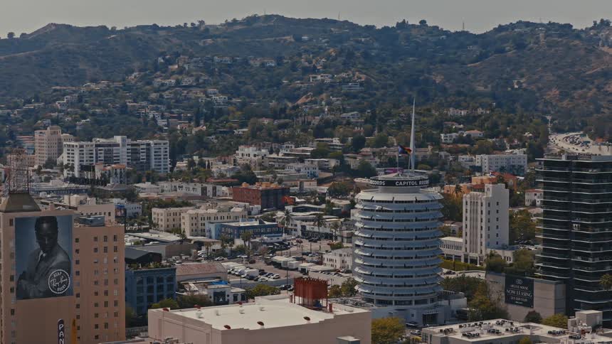 A high-angle view of the iconic Capitol Records Building and Hollywood with the rolling hills in the background during the day
