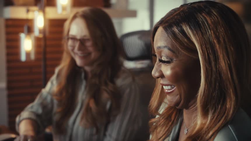 Close-up of two diverse female colleagues happily collaborating on a project in a modern, warmly lit office