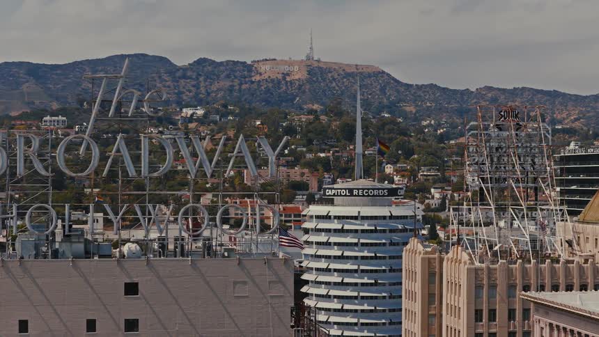 An iconic view over the rooftops of Hollywood, featuring the Capitol Records building and the famous Hollywood sign in the distant hills
