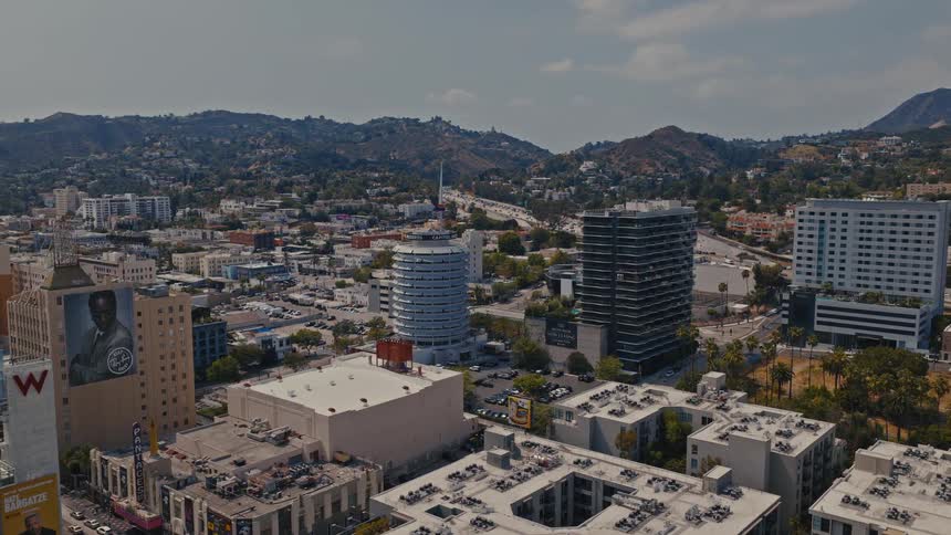 An aerial view pulls back to reveal the iconic Capitol Records Building and the sprawling cityscape of Hollywood, with the Hollywood Hills in the distance