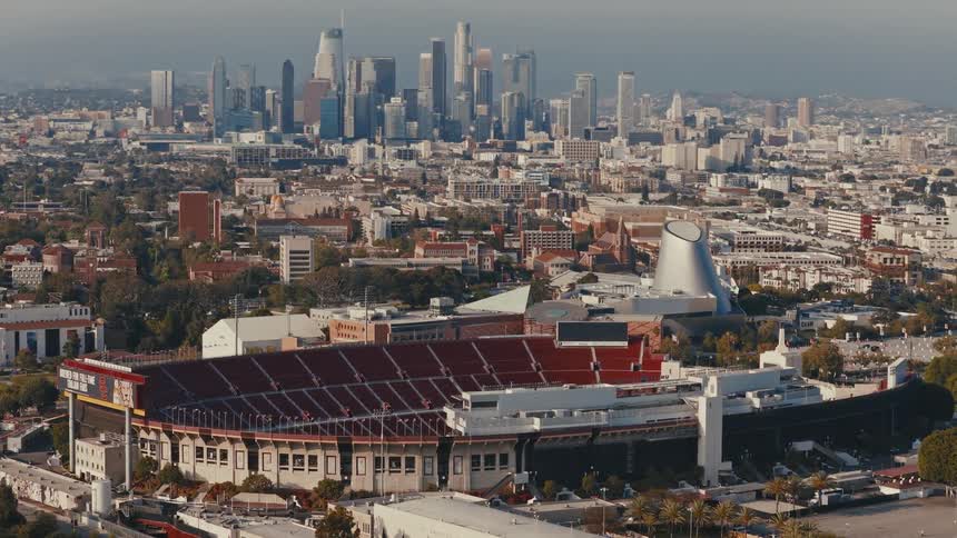 An aerial view of the Los Angeles Memorial Coliseum and the California Science Center with the downtown LA skyline in the background