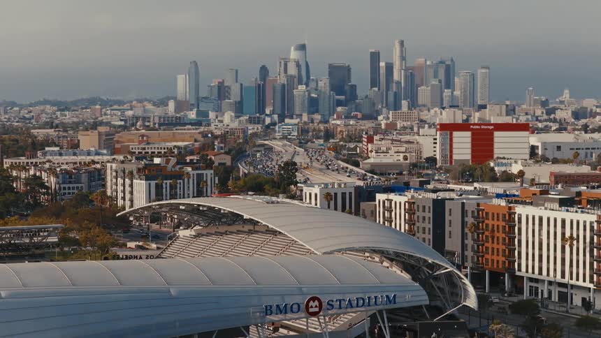 Slow aerial pan showing the BMO Stadium in the foreground with the downtown Los Angeles skyline and highway in the background