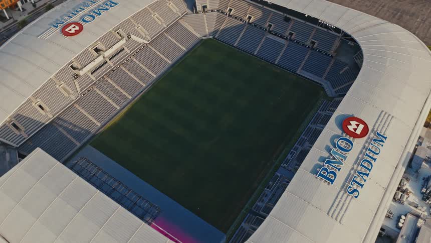 A slow, orbiting aerial shot showcases the modern architecture of the empty BMO Stadium on a bright day