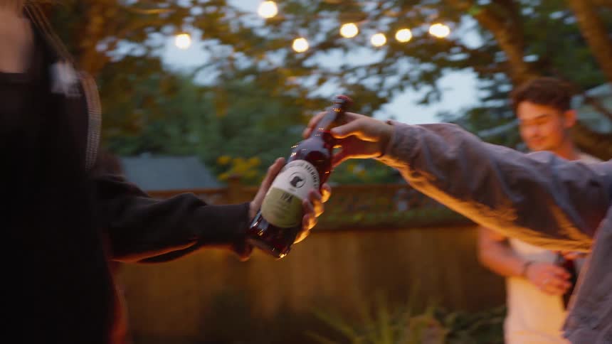 A young woman grabs a beer from a cooler and hands it to her friend at a backyard party