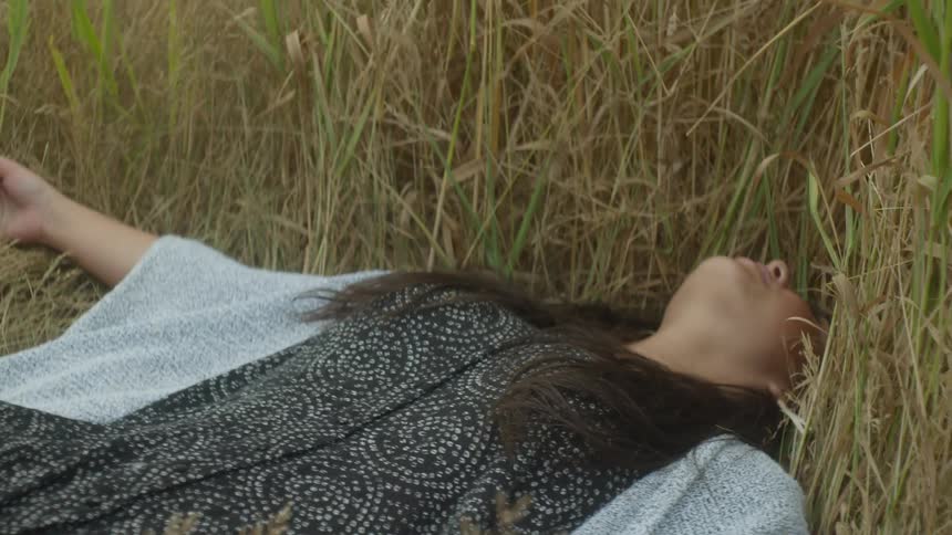 Close up of a beautiful young woman with long dark hair lying down in a tall grassy field