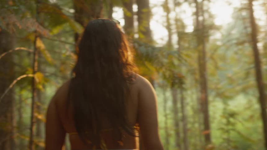 A happy woman in a bikini walks through a sun-kissed forest and stops to admire the golden light
