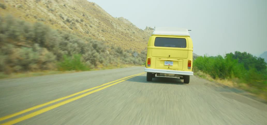 A point of view shot reveals a classic yellow camper van driving down a rural two-lane highway