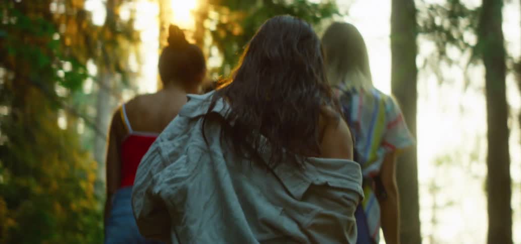 A slow-motion shot from behind a diverse group of young women as they walk through a sun-drenched forest during golden hour
