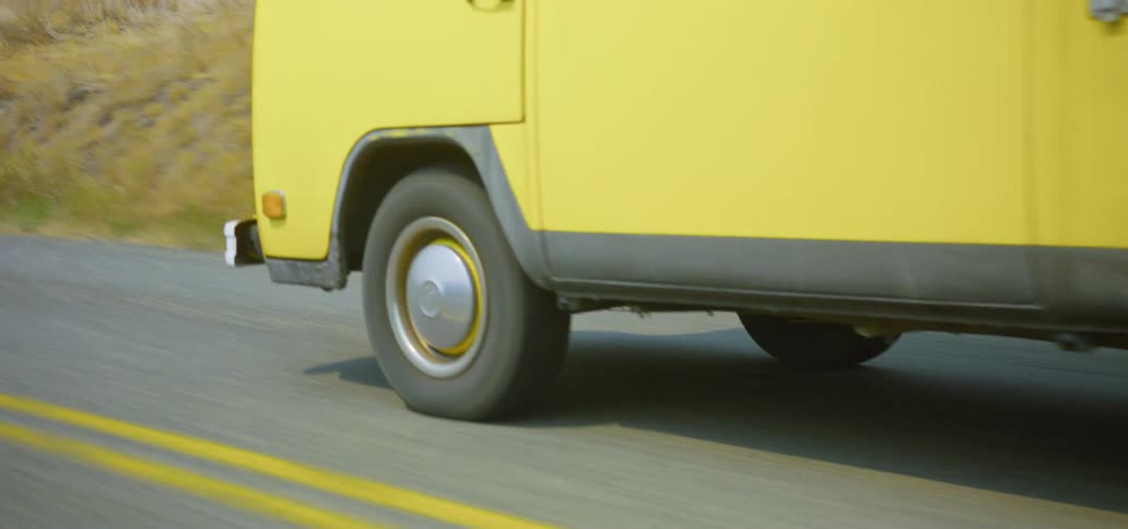 A vintage yellow Volkswagen camper van drives along a winding country road on an adventurous road trip