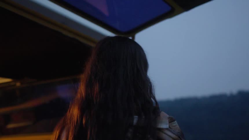 A young woman in slow motion opens the back of her yellow camper van at dusk, grabs her toothbrush, and begins her nightly routine while camping in nature