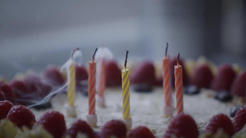 A lighter is used to extinguish the flames on colorful birthday candles in slow motion, leaving wisps of smoke