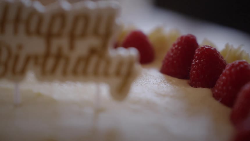 A close-up slow-motion shot of a hand carefully placing a fresh raspberry on a white frosted birthday cake