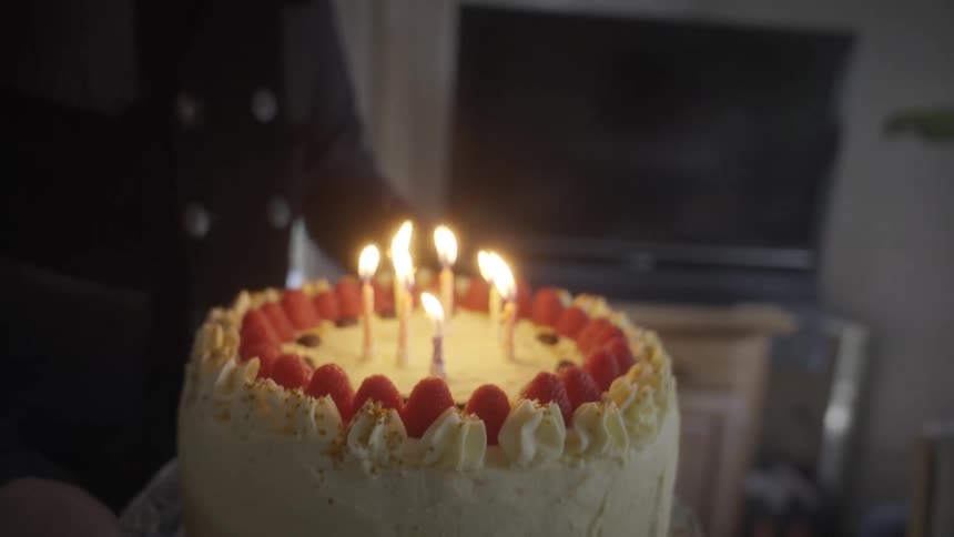 Close-up slow-motion shot of a person bringing a raspberry birthday cake with burning candles into a room for a celebration