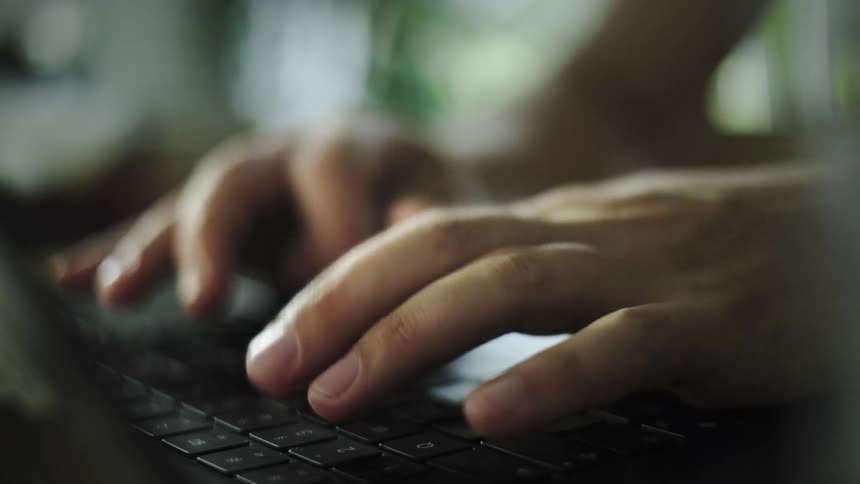 A close-up side view of a person's hands typing on a laptop keyboard in a dimly lit setting