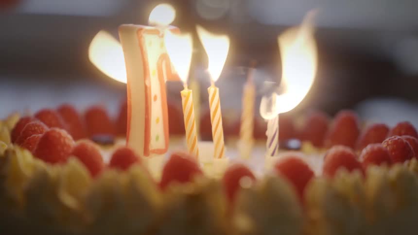 A close-up of someone blowing out the lit number seven candle on a raspberry birthday cake