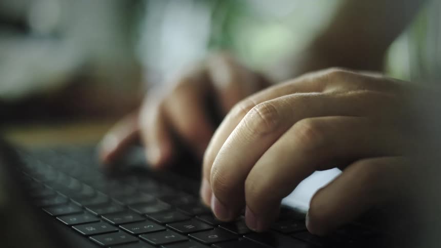 A dramatic close-up of a person's hands typing on a laptop keyboard in a moody setting