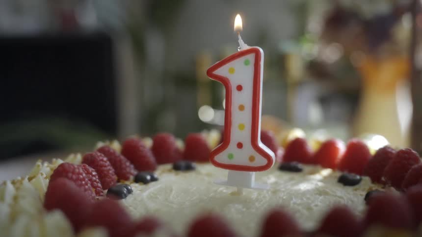 A hand uses a lighter to light a number one candle on a raspberry birthday cake in slow motion