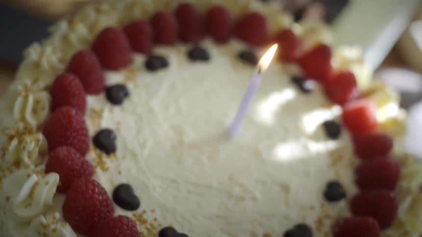 Close-up of a single lit purple candle burning on a beautifully decorated birthday cake with raspberries and chocolate hearts
