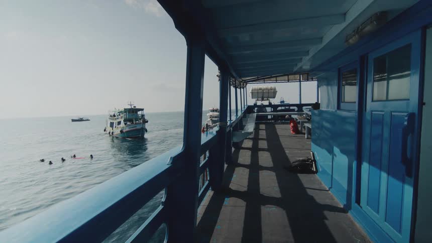 View from a dive boat deck as snorkelers swim in the calm ocean with another boat nearby