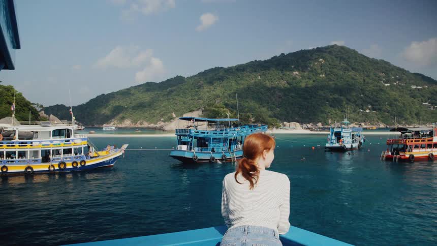 Back view of a redhead woman on a boat trip looking at the beautiful scenery of a tropical island and other tour boats in the bay