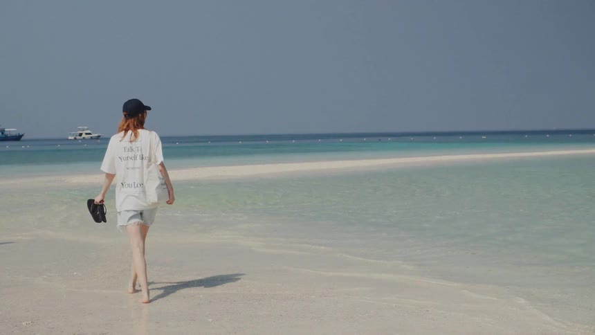 A woman walks in slow motion along a beautiful white sandbar surrounded by the clear turquoise ocean