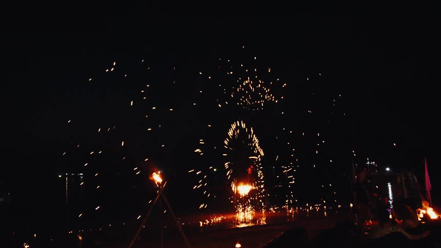 A fire dancer spins a sparkling prop in slow motion, creating a mesmerizing shower of light at a night festival