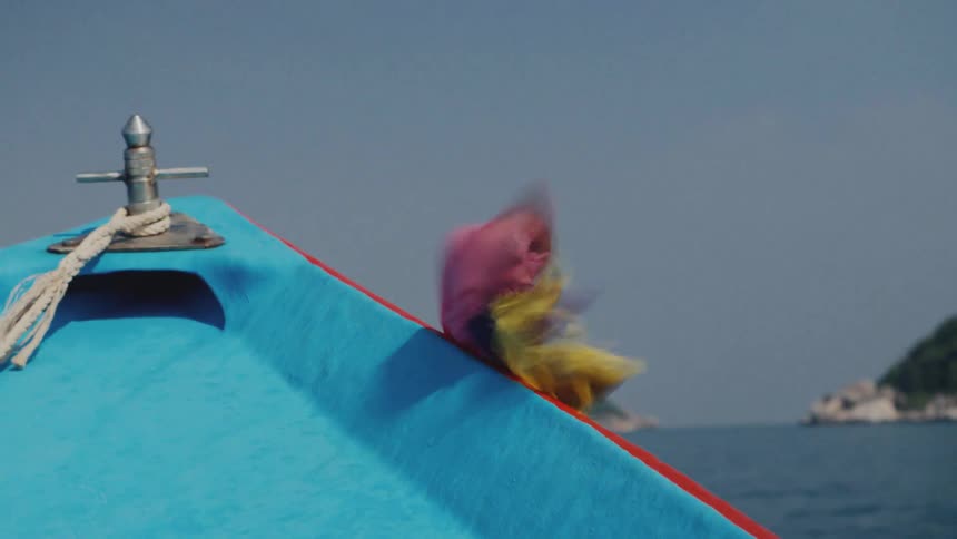 Colorful ribbons blow in the wind on the bow of a long-tail boat as it sails across the ocean towards a tropical island