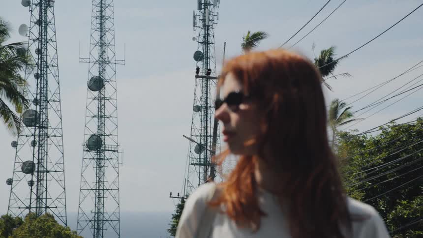 Portrait of a woman with red hair and sunglasses as the focus shifts from communication towers in the background
