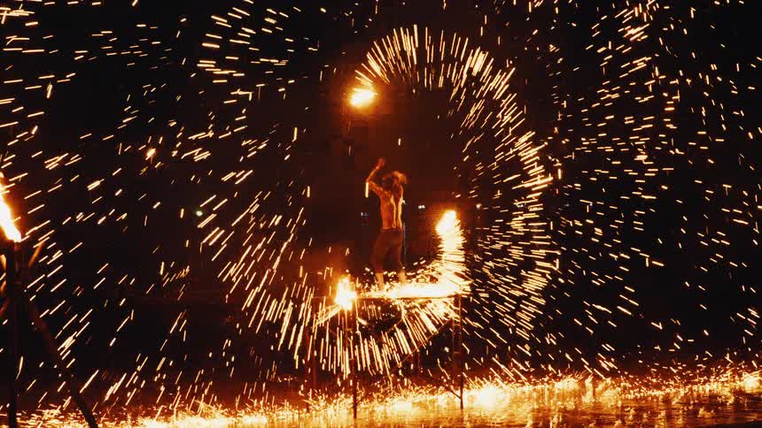 A skilled fire dancer performs a mesmerizing show at night, spinning a flaming staff to create a brilliant spiral of sparks