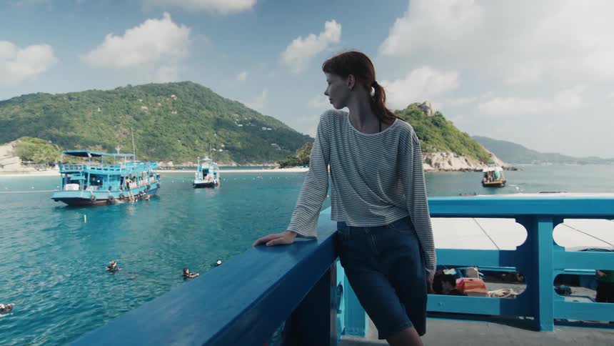 A young woman thoughtfully gazes out from a boat at a stunning tropical bay filled with tour boats and divers