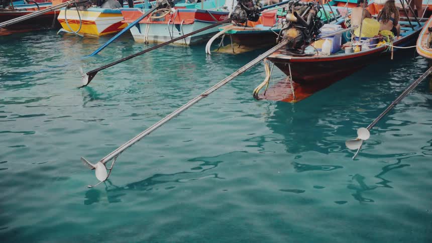 Close-up of propellers on traditional Thai longtail boats docked in the vibrant turquoise water of a busy harbor
