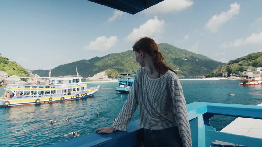 A woman on a tour boat looks out at a stunning tropical island bay with swimmers and boats in the turquoise water