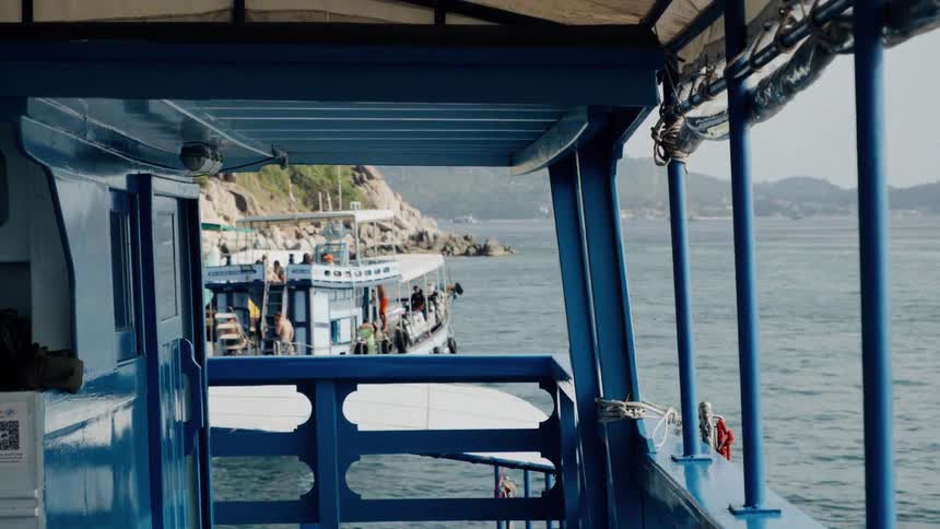 A tranquil view from a blue boat's deck reveals another tour boat anchored near a rocky tropical island