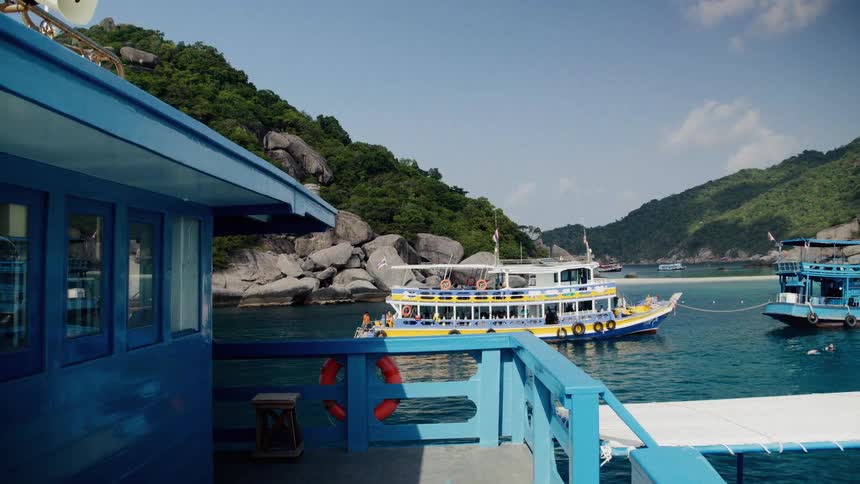 Colorful tour boats are anchored in a beautiful turquoise bay surrounded by lush green hills in Thailand