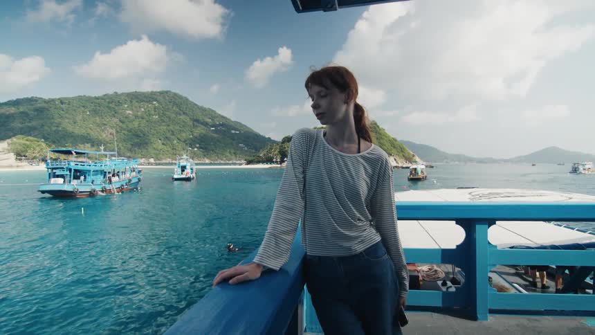 A thoughtful young woman on the railing of a boat looks out over a beautiful tropical sea