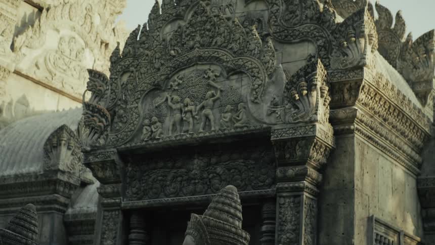 A tilt-up shot reveals the intricate stone carvings and weathered statues of an ancient Southeast Asian temple