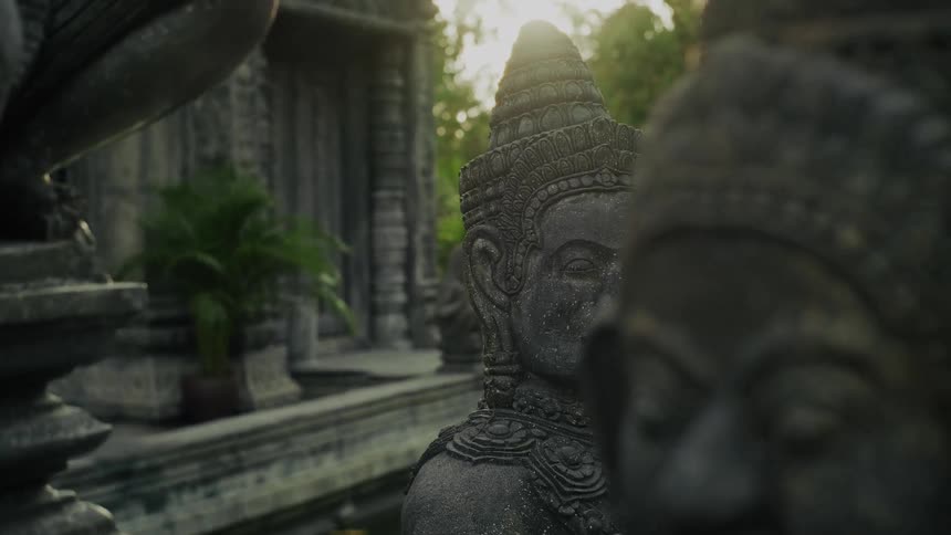 A slow, cinematic pan reveals ancient stone statues guarding a tranquil Asian temple at golden hour