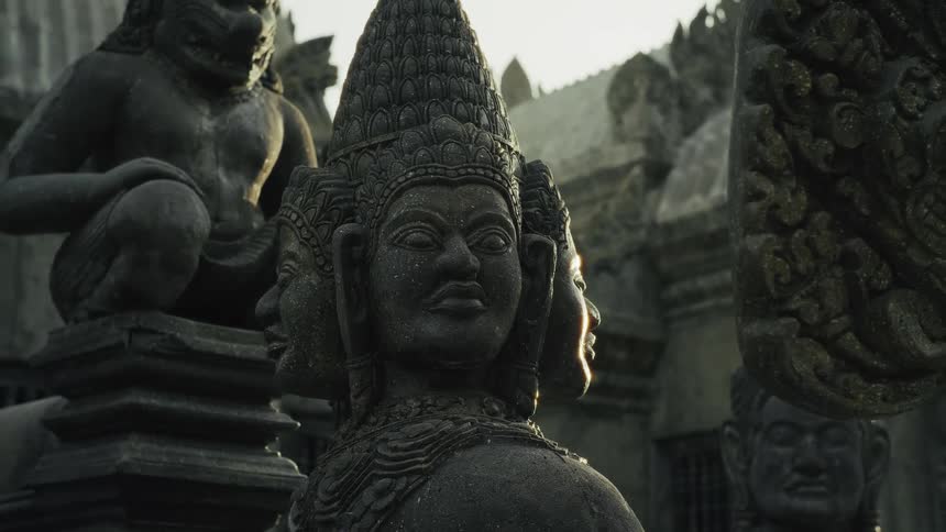 Mystical golden hour light reveals ancient, weathered stone statues of Hindu deities at a Khmer temple
