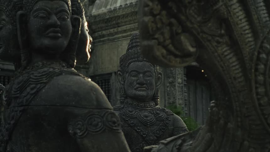 Intricately carved stone statues of deities at an ancient temple are illuminated by a warm sun flare