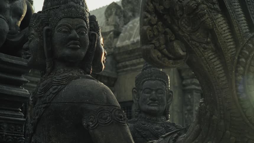 Ancient and mystical stone statues of deities stand guard at a temple, bathed in the golden light of the sun