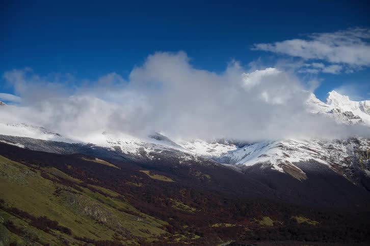 A stunning timelapse of white clouds swirling around a majestic, snow-capped mountain peak against a vibrant blue sky