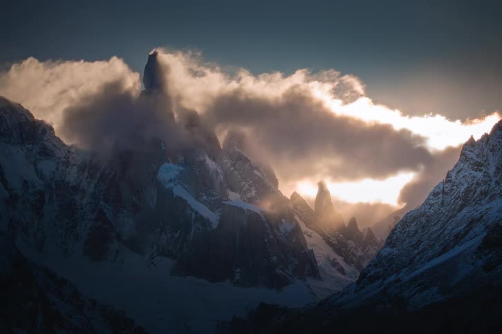 Golden clouds move across the jagged snow-capped peaks of a majestic mountain range at sunrise