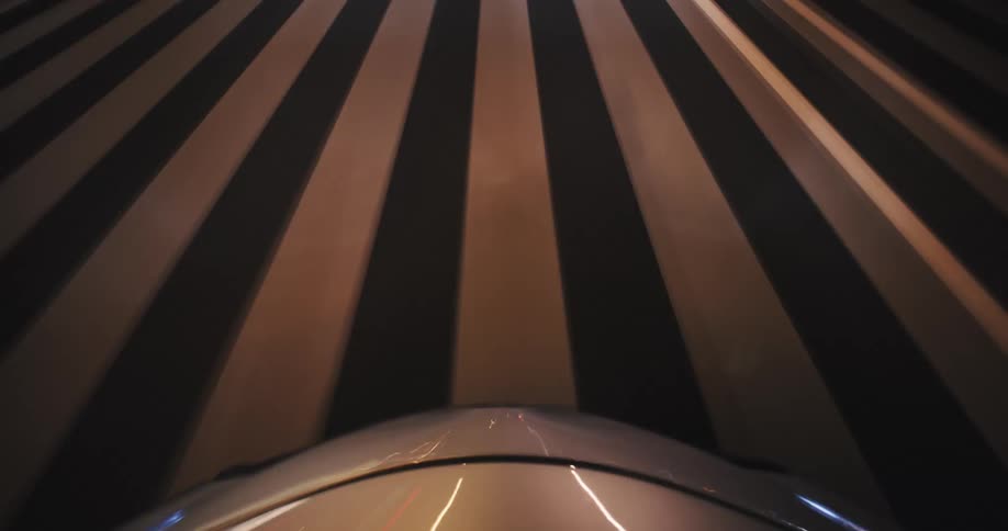 A surreal time-lapse from a car's hood captures the blur of lights and road markings while speeding through a city tunnel at night