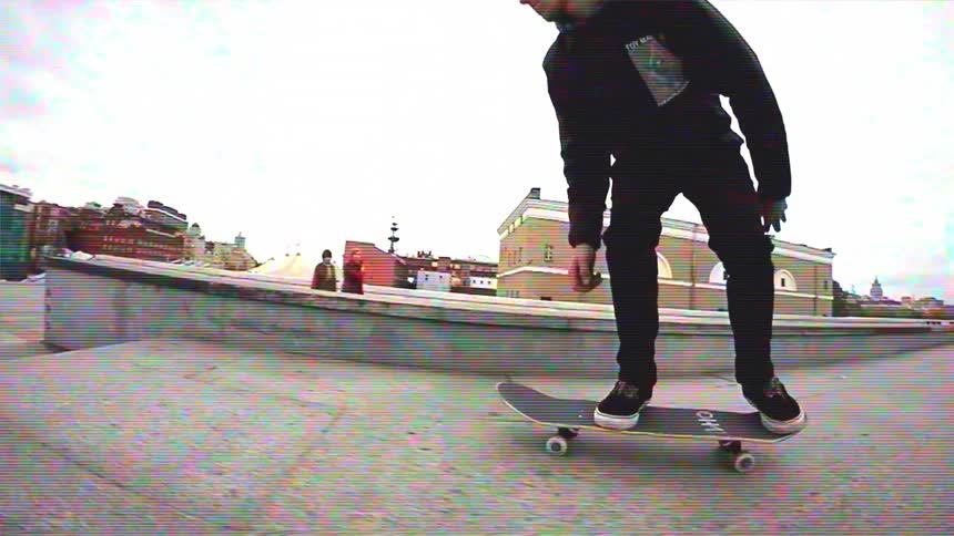 A skateboarder in a black hoodie performs a series of tricks on a city ledge, filmed in slow motion with a retro VHS effect