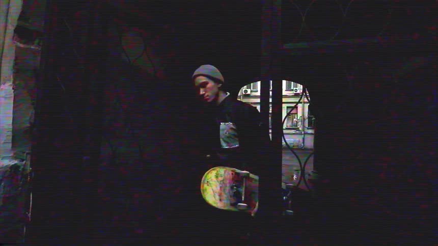 Slow-motion footage with a VHS glitch effect shows a skater walking through a dark urban archway towards the camera