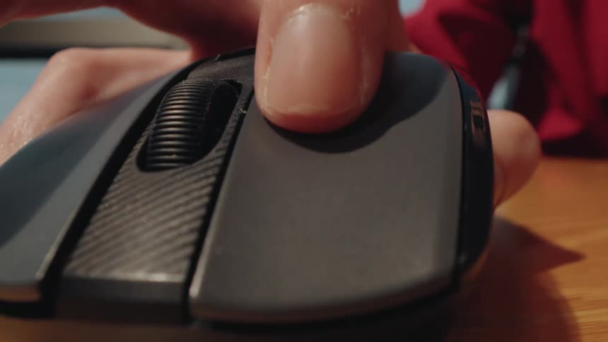 Extreme close-up of a hand in a red shirt clicking a wireless computer mouse on a wooden desk