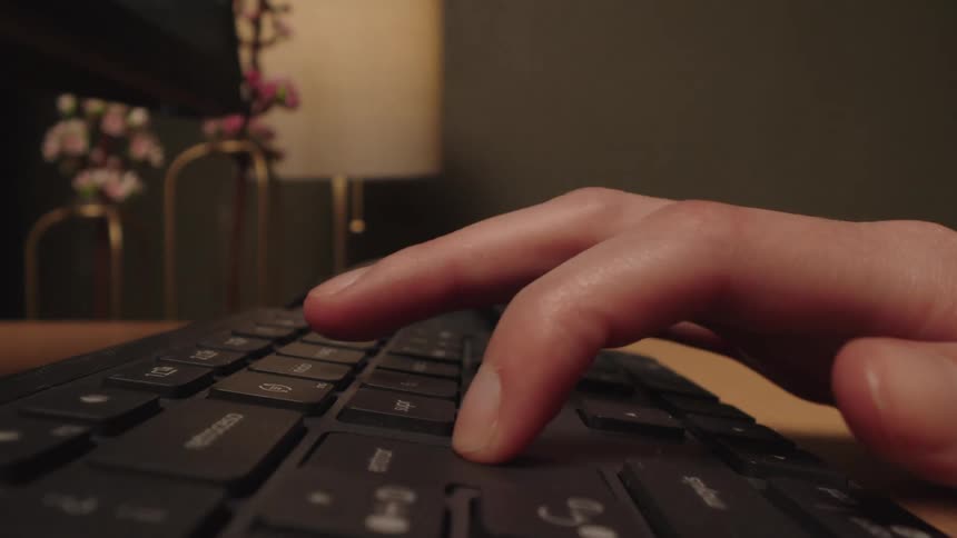 A person's hand types and then presses the enter key on a computer keyboard in a close-up, low-angle shot